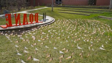 Cassel Outdoor Theatre on Doane’s Crete campus has nearly 700 orange pennants on display atop the green grass. Giant letters reading G-O D-O-A-N-E can be seen near the pennants. 